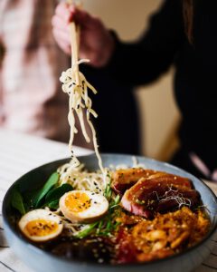 Eine Person isst Ramen mit Stäbchen mit unterschiedlichen Toppings
