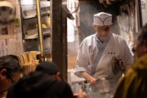 Ein japanischer Koch bereitet dampfende Ramen in einer Küche für arbeitende Menschen zu